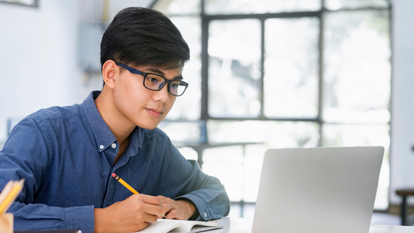 man in blue shirt and glasses looking at a laptop and taking notes