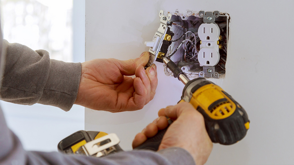 person with power drill fixing an electrical outlet