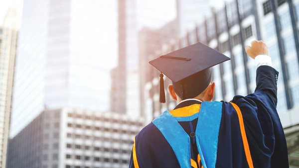 man in a graduate cap and gown holding his fist up in a city