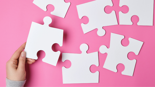 hand holding a puzzle piece on a pink background