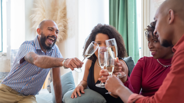 Two men and two women all cheers glasses of wine together.