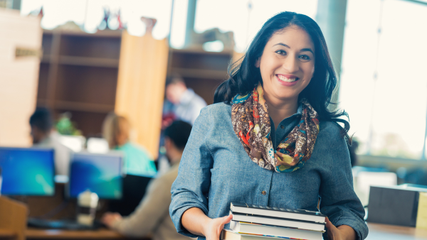 A woman holding a stack of books while smiling. 