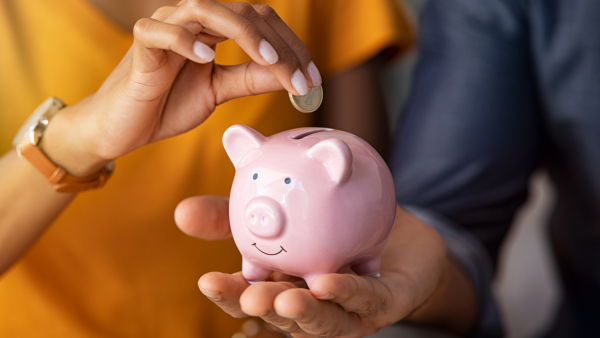 Woman inserting coin into piggy bank.