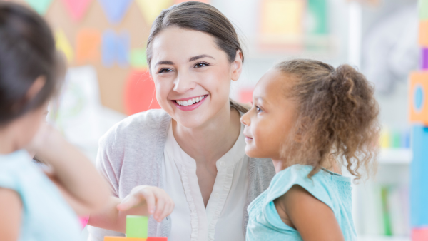 A woman smiling with a toddler next to her. 